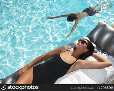 Woman tanning by the pool, man swimming