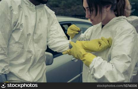 Woman taping bacteriological protective suit gloves to a man outdoors. Woman taping bacteriological protective gloves to a man