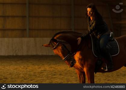 Woman taps the horse in indoor arena, woman looks toward the horse, horizon format