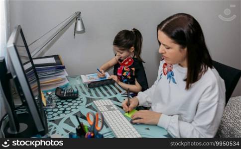 Woman teleworking with her daughter drawing side by side. Selective focus on girl in background. Woman teleworking with her daughter drawing