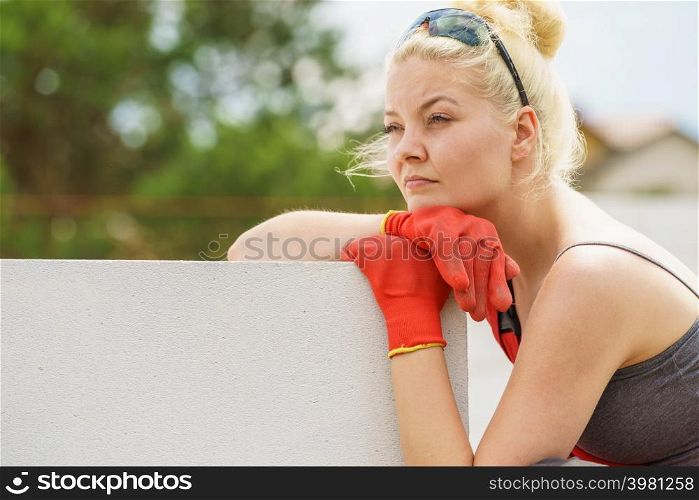 Woman thinking about future of building her home. Female sitting on wall made of airbricks on construction site contemplating. Woman taking break on construction site