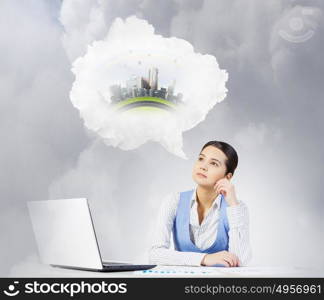 Woman thinking over her project. Beautiful woman sitting at table with laptop and dreaming