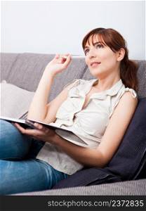 Woman thinking sitting on couch holding a pen and a book