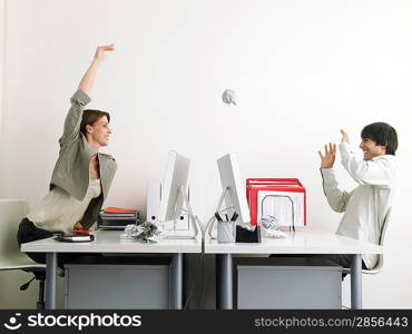 Woman throwing paper at man in office side view