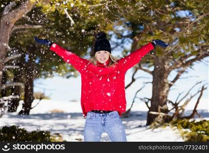 Woman throwing snowballs in a snowy forest in the mountains, in Sierra Nevada, Granada, Spain. Female wearing winter clothes playing with snow.. Woman throwing snowballs in a snowy forest in the mountains