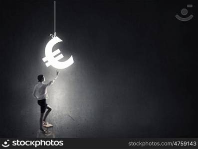 Woman touch euro symbol. Young attractive businesswoman standing on chair and reaching euro sign