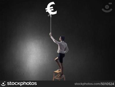 Woman touch euro symbol. Young attractive businesswoman standing on chair and reaching euro sign
