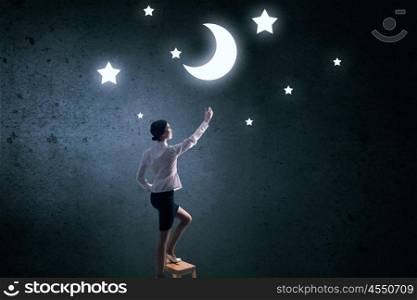 Woman touch the moon. Young woman standing on chair and reaching moon