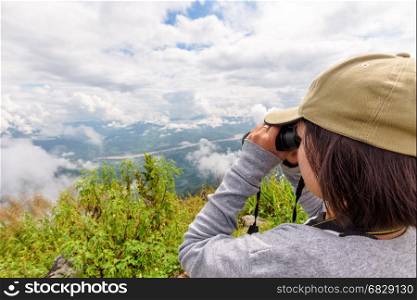 Woman tourist are using binoculars to see the beautiful natural landscape of the sky forest and mountain near the Mekong River at Doi Pha Tang view point in Chiang Rai Province, Thailand