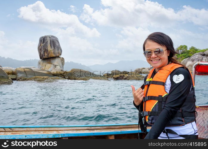 Woman tourist in life vest wearing sunglasses on the boat thumb up for the beautiful of the sea and nature in summer at Ko Hin Sorn stone island near Ko Lipe at Tarutao National Park, Satun, Thailand. Woman on the boat at Ko Hin Sorn island in Thailand