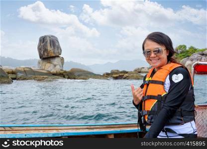 Woman tourist in life vest wearing sunglasses on the boat thumb up for the beautiful of the sea and nature in summer at Ko Hin Sorn stone island near Ko Lipe at Tarutao National Park, Satun, Thailand. Woman on the boat at Ko Hin Sorn island in Thailand