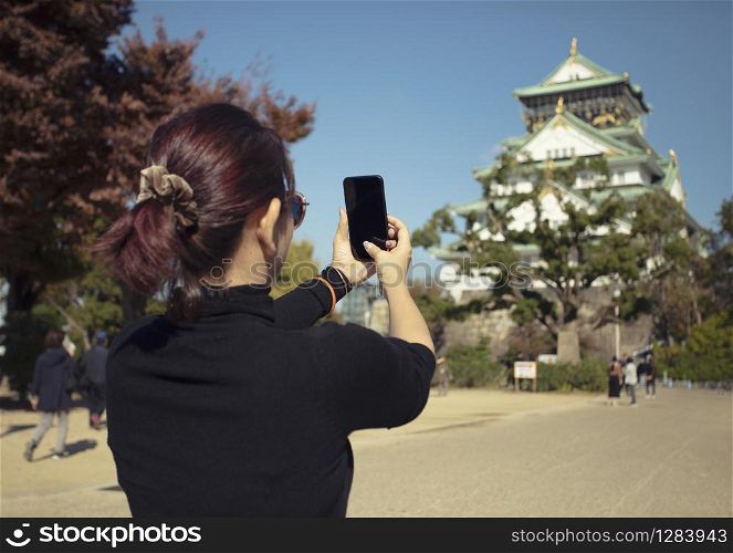 woman tourist taking a photo of osaka castle by smart phone,osaka castle is one of most popular traveling destination in japan