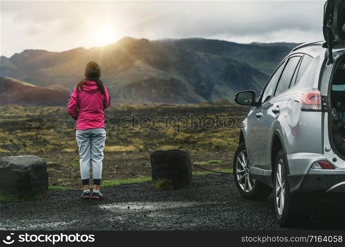 Woman tourist travel by SUV car for road trip in Iceland. The traveler parking the car and enjoy beautiful scenery of mountain landscape in the background. Discovery and exploration.
