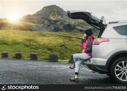 Woman tourist travel by SUV car for road trip in Iceland. The traveler parking the car and enjoy beautiful scenery of mountain landscape in the background. Discovery and exploration.