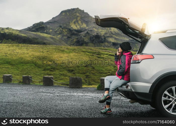 Woman tourist travel by SUV car for road trip in Iceland. The traveler parking the car and enjoy beautiful scenery of mountain landscape in the background. Discovery and exploration.