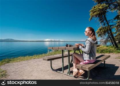 Woman tourist with camera having a breakfast by Yellowstone Lake, Wyoming, USA
