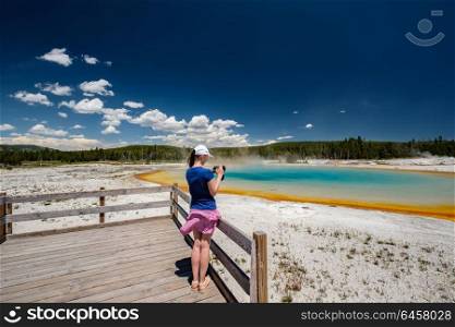 Woman tourist with camera overlooking hot thermal spring Sunset Lake in Yellowstone National Park, Black Sand Basin area, Wyoming, USA
