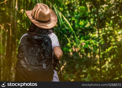 Woman tourist with hat and backpack standing in evergreen forest. Alone young woman traveller enjoy travel.