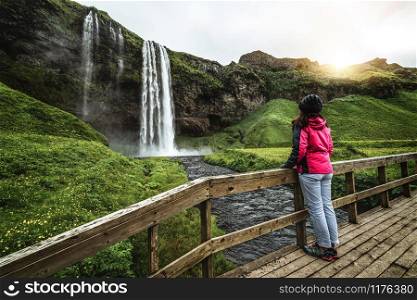 Woman traveler at Magical Seljalandsfoss Waterfall in Iceland located near ring road of South Iceland. Majestic and picturesque, it is one of most photographed breathtaking place of Iceland wilderness