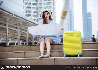 Woman traveler tourism with travel suitcase on vacation summer dream asian destination holding map for tourist looking on journey voyage sitting in modern city. travel and journey lifestyle concept.