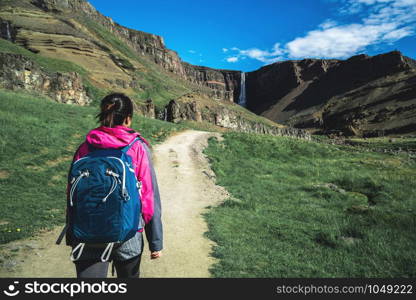 Woman traveler trekking in Icelandic summer landscape at the Hengifoss waterfall in Iceland. The waterfall is situated in the eastern part of Iceland.