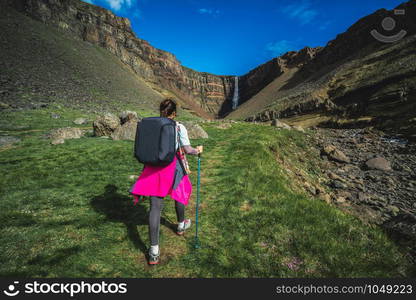 Woman traveler trekking in Icelandic summer landscape at the Hengifoss waterfall in Iceland. The waterfall is situated in the eastern part of Iceland.