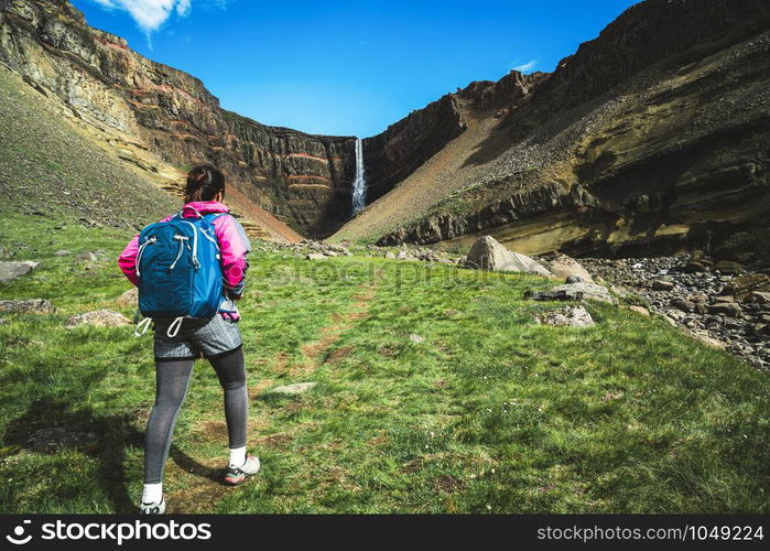 Woman traveler trekking in Icelandic summer landscape at the Hengifoss waterfall in Iceland. The waterfall is situated in the eastern part of Iceland.