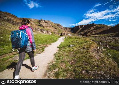 Woman traveler trekking in Icelandic summer landscape at the Hengifoss waterfall in Iceland. The waterfall is situated in the eastern part of Iceland.