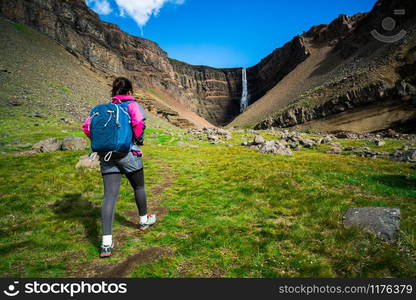 Woman traveler trekking in Icelandic summer landscape at the Hengifoss waterfall in Iceland. The waterfall is situated in the eastern part of Iceland.