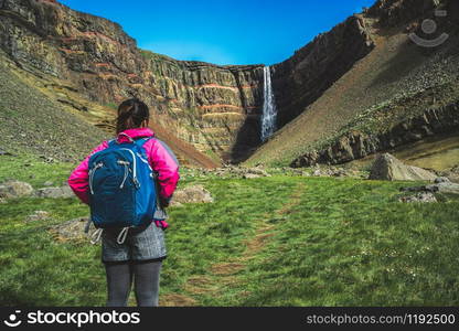 Woman traveler trekking in Icelandic summer landscape at the Hengifoss waterfall in Iceland. The waterfall is situated in the eastern part of Iceland.