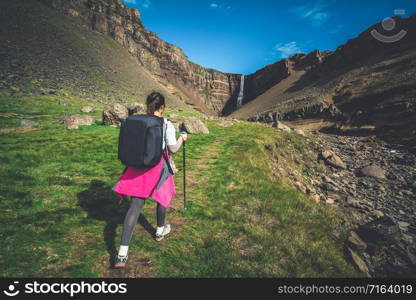 Woman traveler trekking in Icelandic summer landscape at the Hengifoss waterfall in Iceland. The waterfall is situated in the eastern part of Iceland.