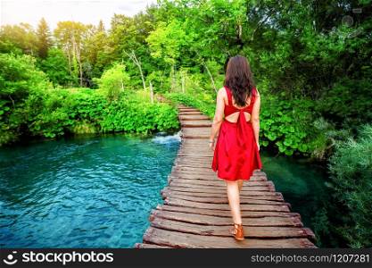 Woman traveler walking on wooden path trail with lakes and waterfall landscape in Plitvice Lakes National Park, UNESCO natural world heritage and famous travel destination of Croatia.. Traveler walk on path in Plitvice Lakes, Croatia.