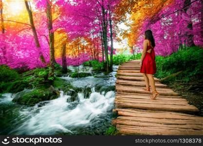 Woman traveler walking on wooden path trail with lakes and waterfall landscape in Plitvice Lakes National Park, UNESCO natural world heritage and famous travel destination of Croatia.. Traveler walk on path in Plitvice Lakes, Croatia.