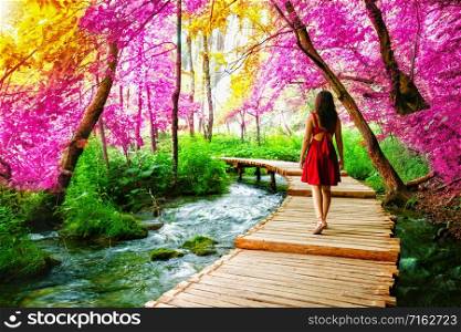 Woman traveler walking on wooden path trail with lakes and waterfall landscape in Plitvice Lakes National Park, UNESCO natural world heritage and famous travel destination of Croatia.