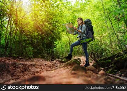 woman traveler with backpack and map searching directions in the natural forest