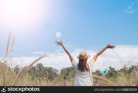 woman traveler with camera holding hat and breathing at field of grasses and forest, wanderlust travel concept, space for text, atmosperic epic moment