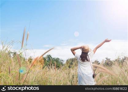 woman traveler with camera holding hat and breathing at field of grasses and forest, wanderlust travel concept, space for text, atmosperic epic moment