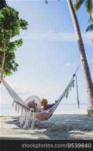Woman traveller in summer hat relaxing on hammock and holding a coconut fruit on the beach