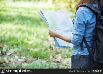 Woman traveller using map in green natural park trekking alone happy, carefree enjoy backpack outdoor lifestyle. Asian woman traveler wanderlust in dream destination with backpack hipster journey