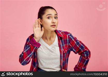 Woman tries to hear, pink background, emotion. Face expression, female person looking on camera in studio, emotional concept, feelings. Woman tries to hear, pink background, emotion