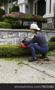 Woman trimming hedges with electric Shares at home