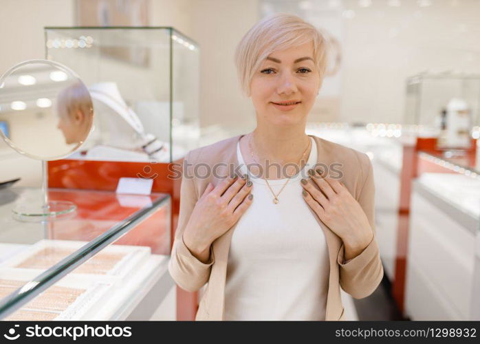 Woman trying on golden necklace at the showcase in jewelry store. Female person buying gold decoration in jewellery shop