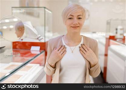 Woman trying on golden necklace at the showcase in jewelry store. Female person buying gold decoration in jewellery shop
