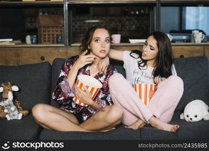woman trying take popcorn from her friend s bucket while watching television