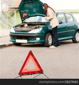 Woman trying to fix her broken car breakdown sign triangle