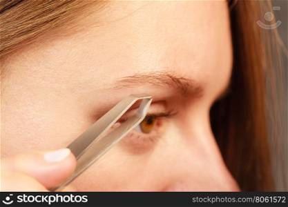Woman tweezing eyebrows depilating with tweezers. Woman plucking eyebrows depilating with tweezers closeup part of face. Girl tweezing eyebrows.