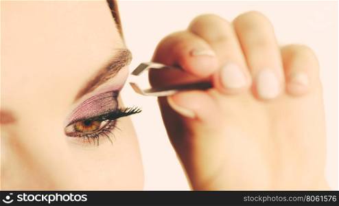 Woman tweezing eyebrows plucking with tweezers . Make up and cosmetics. Woman plucking eyebrows depilating with tweezers. Attractive girl tweezing eyebrows