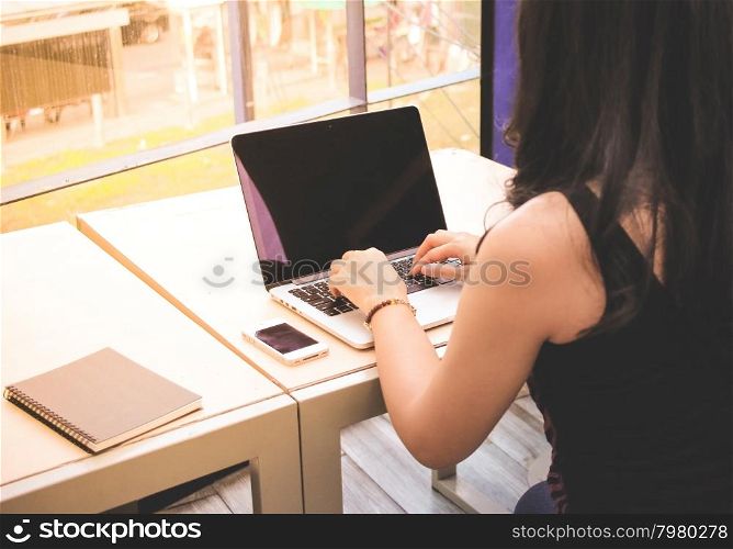 Woman typing keyboard of laptop with smart phone and notebook on the table at home