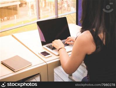 Woman typing keyboard of laptop with smart phone and notebook on the table at home