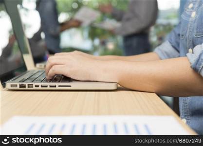 woman typing laptop computer with businessmen discussing with document paperwork in background